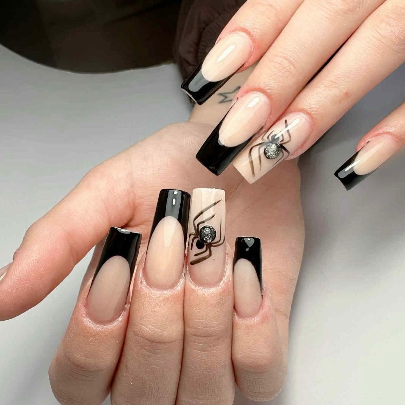 Lange nude nagels met zwarte French tips en een spinnetje als nail art
