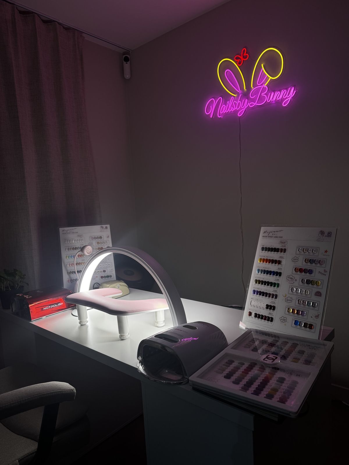 De studio van Nails by Bunny met het roze neonbord met konijnenoortjes, de werktafel en de kleurenkaarten