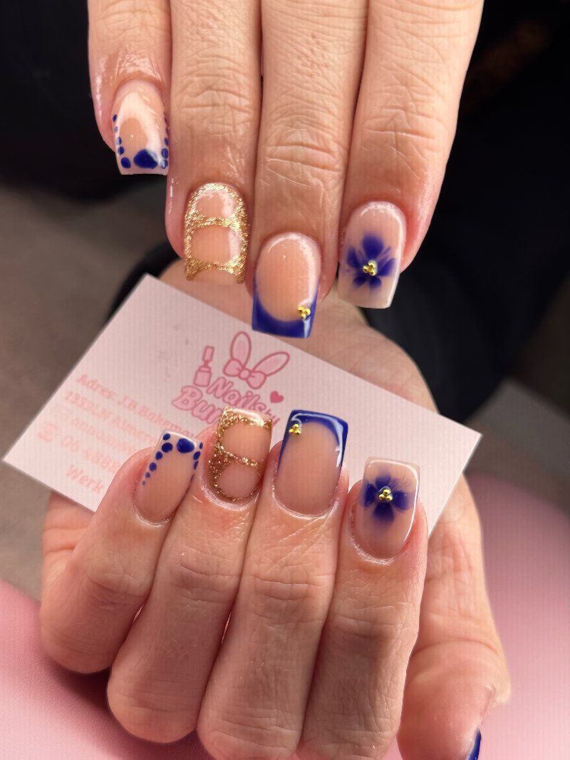 Nude nagels met donkerblauwe French tips, een blauw bloemetje en gouden details